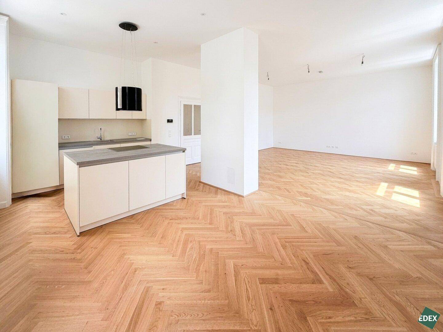 Moderne Einbauküche mit Kochinsel, Induktionskochfeld und Dunstabzugshaube in einem offenen Wohnbereich.