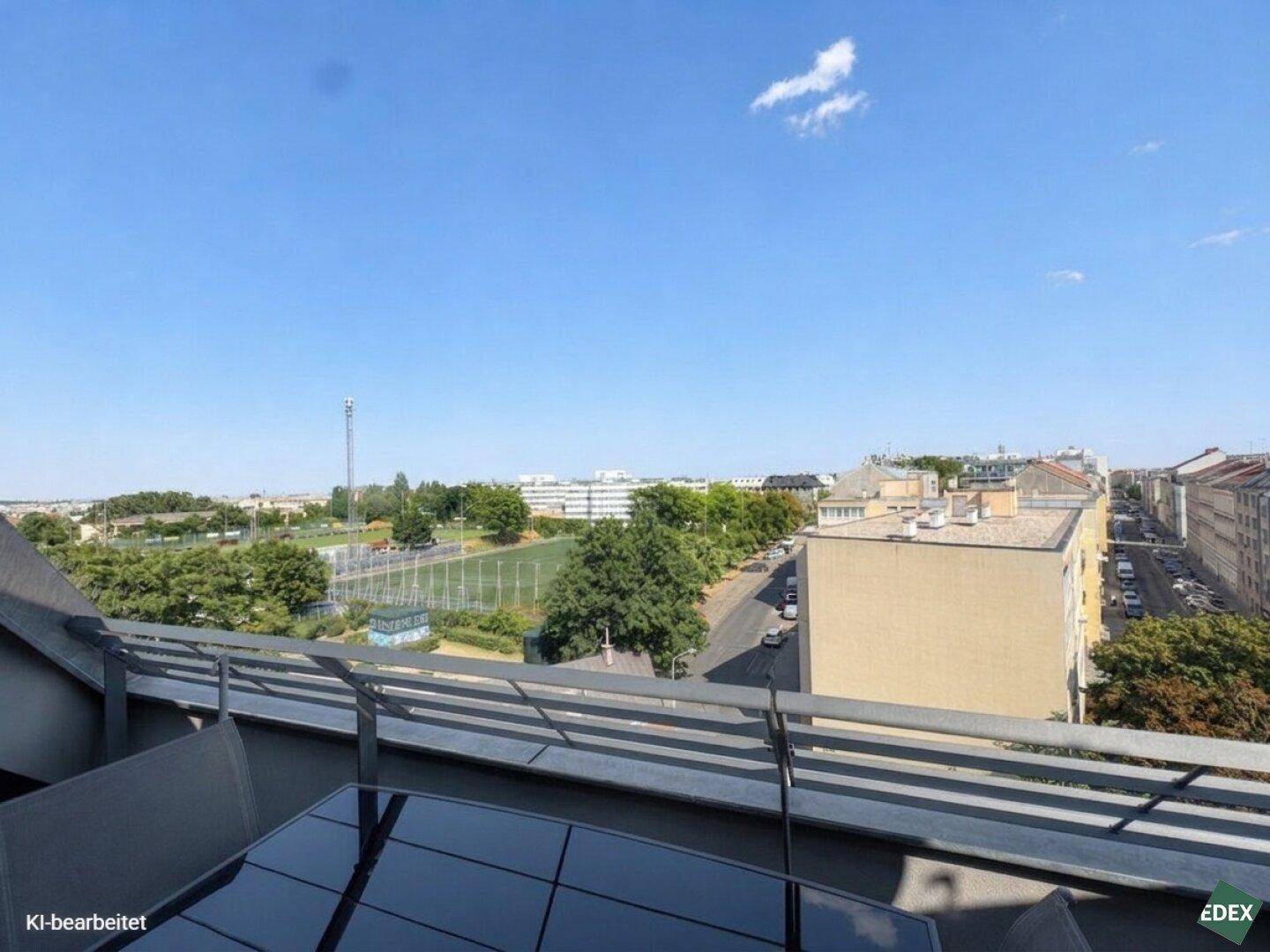 Weitblick von der Terrasse über die Stadt mit Sportplatz und umliegenden Gebäuden.