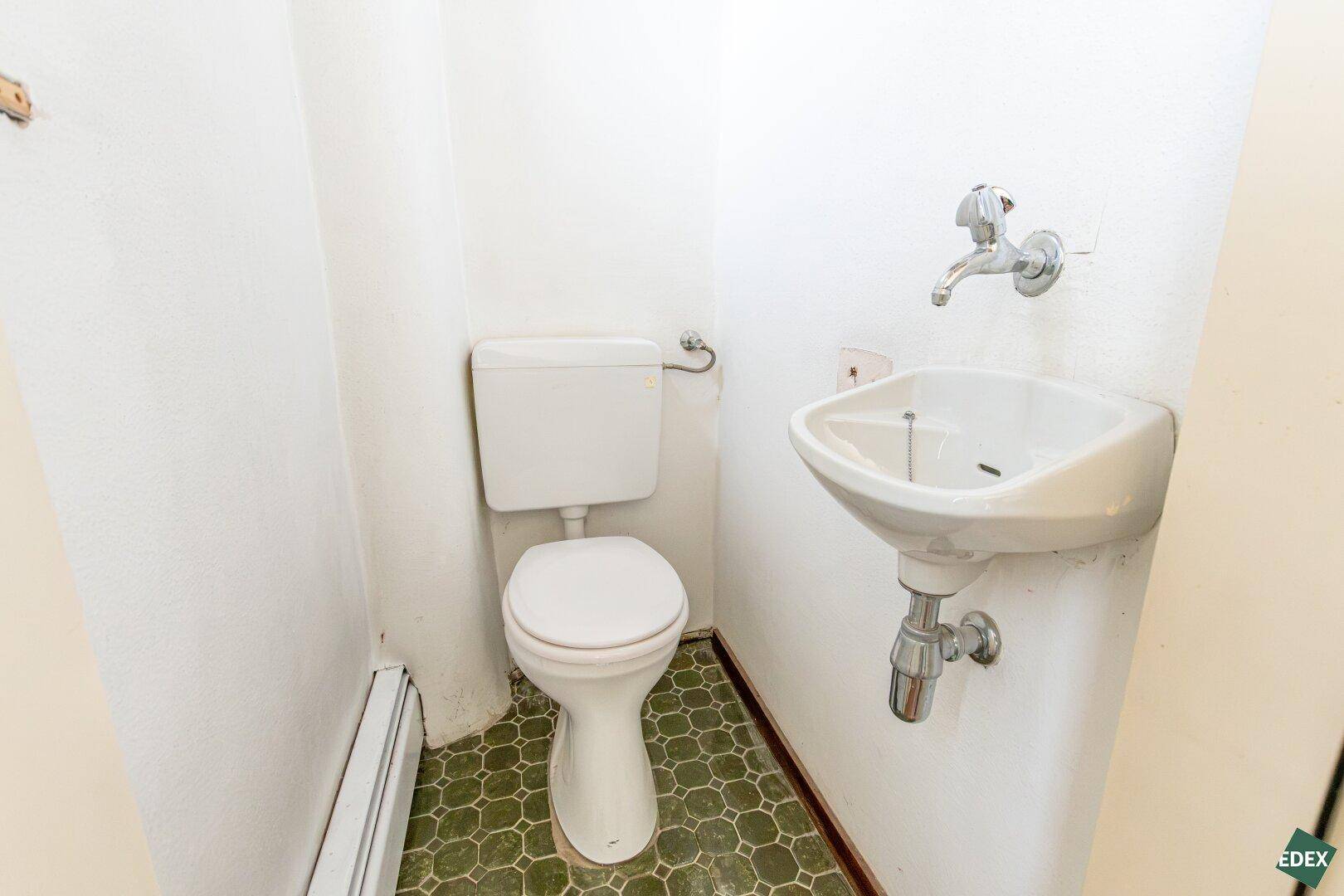 Separate Toilette mit kleinem Waschbecken und Fliesenboden, in einfachem Zustand.