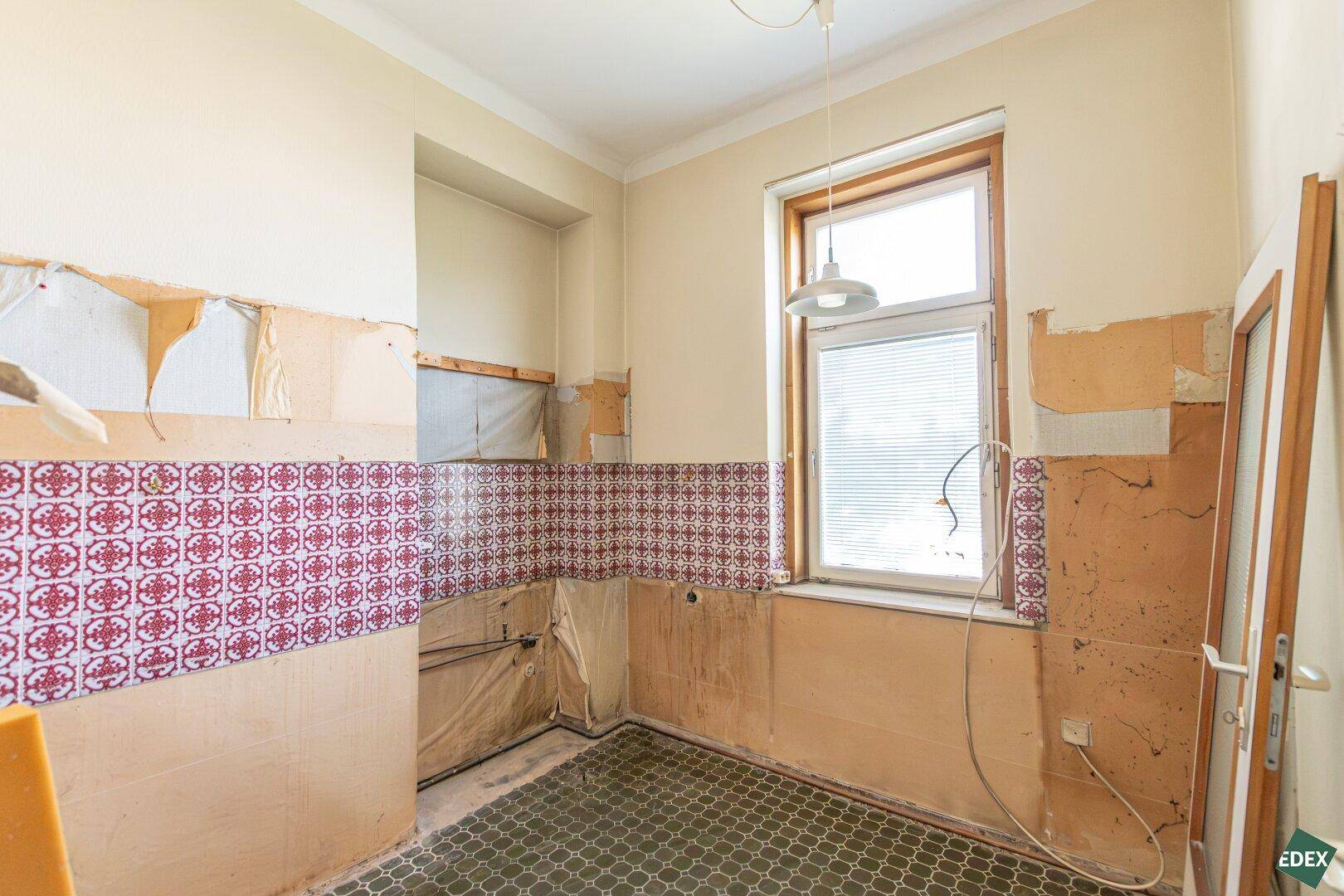 Küche in Renovierung mit alten Fliesen und Fenster, bereit für eine moderne Neugestaltung.