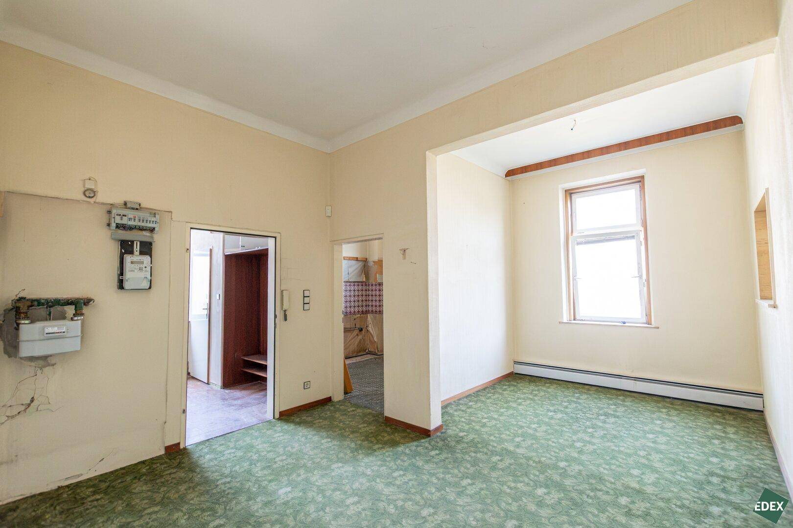 Heller Flur mit grünem Teppichboden und Fenster, der zu verschiedenen Zimmern führt.