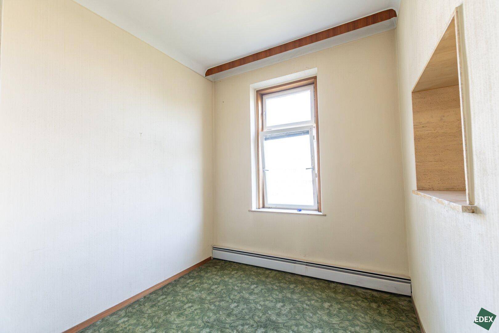 Kleines Zimmer mit grünem Teppichboden und Fenster, ideal als Büro oder Gästezimmer.