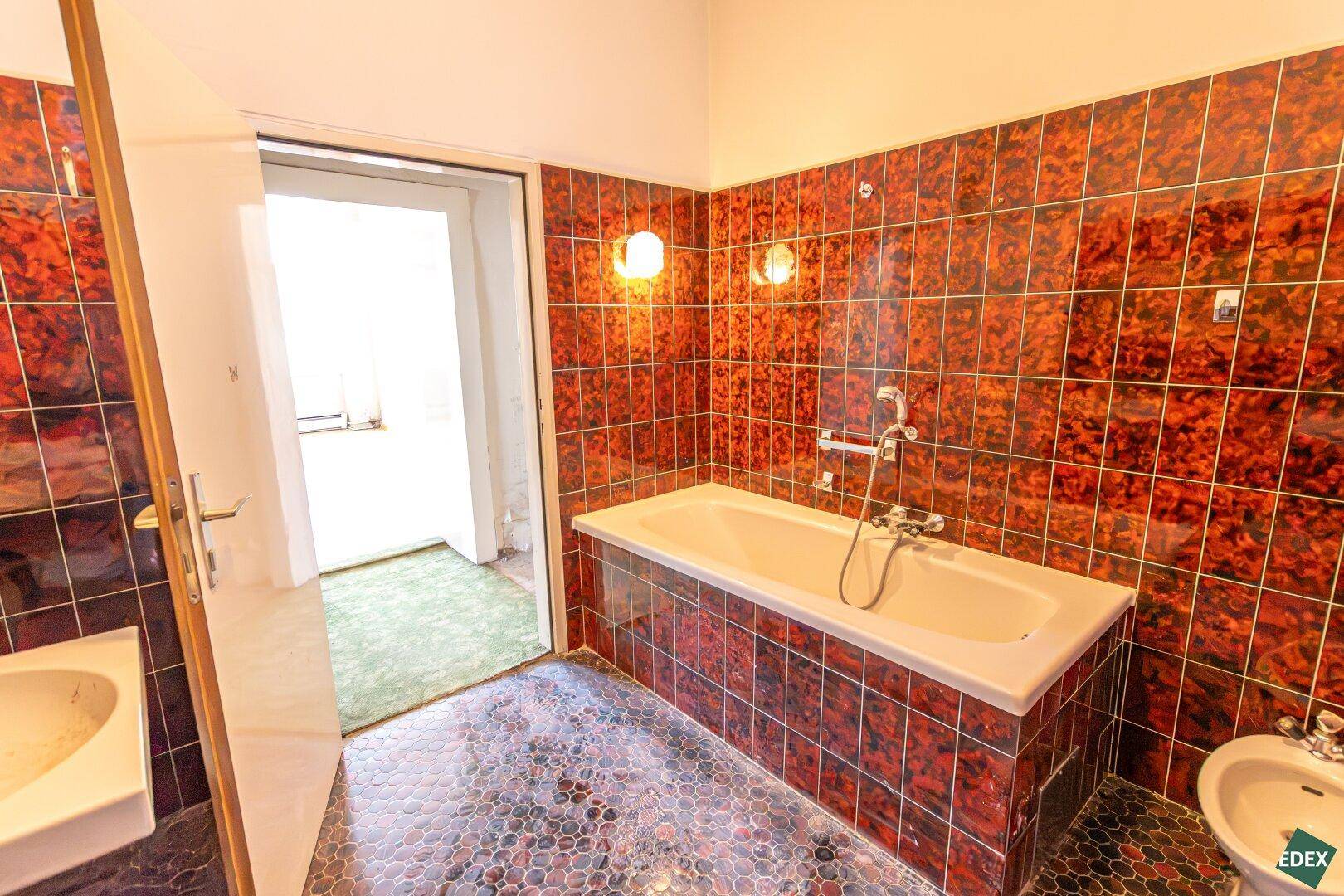 Badezimmer mit auffälligen roten Fliesen, Badewanne und Bidet, das eine Renovierung benötigt.