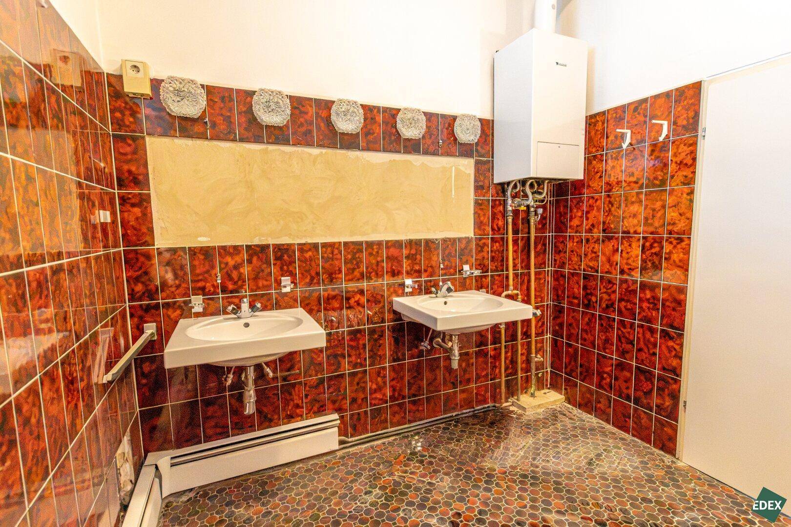 Badezimmer mit roten Fliesen, Doppelwaschbecken und Warmwasserboiler, bereit zur Modernisierung.