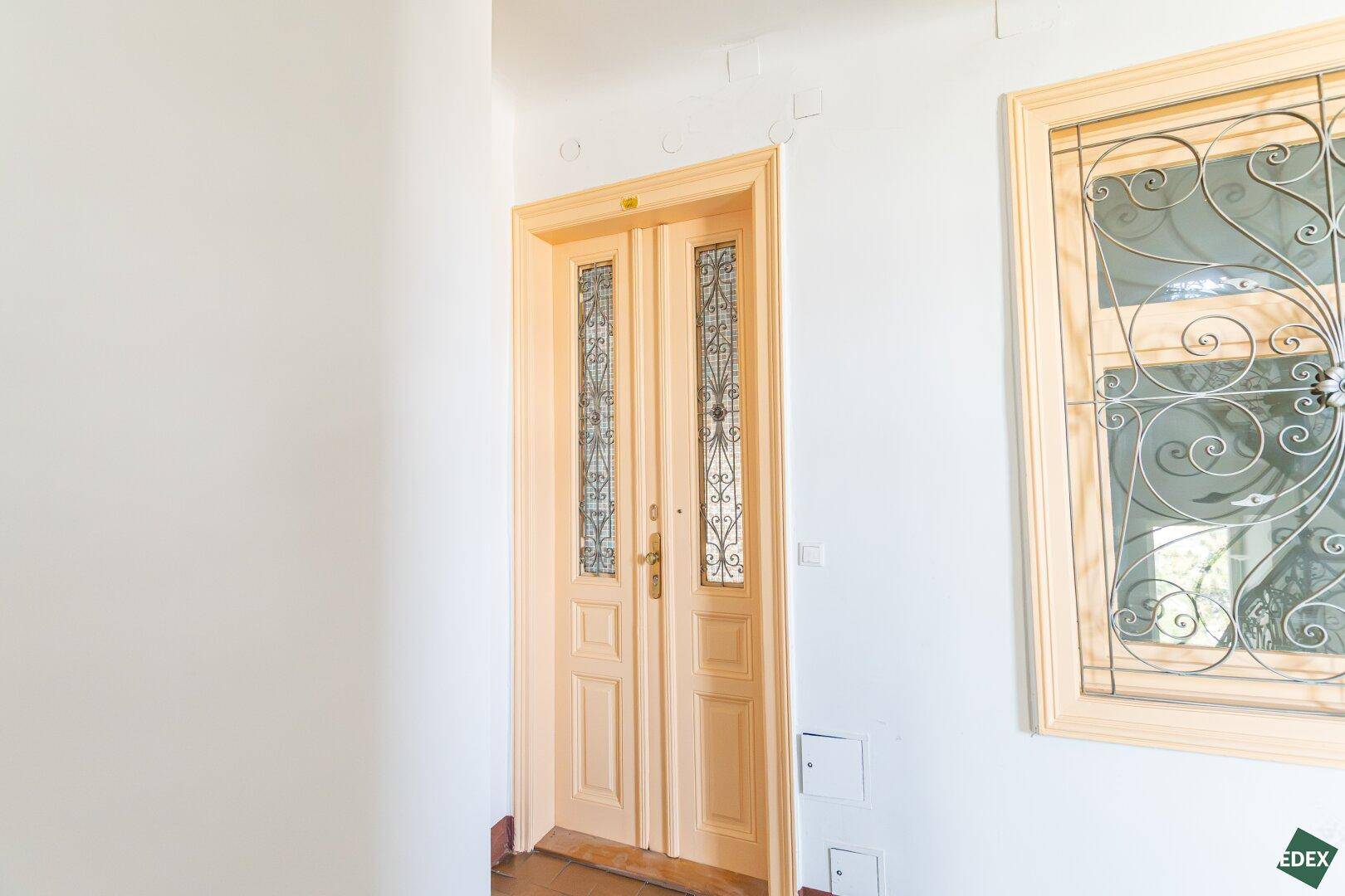 Heller Eingangsbereich mit Holztür und Fenster mit schmiedeeisernem Gitter, klassischer Stil.