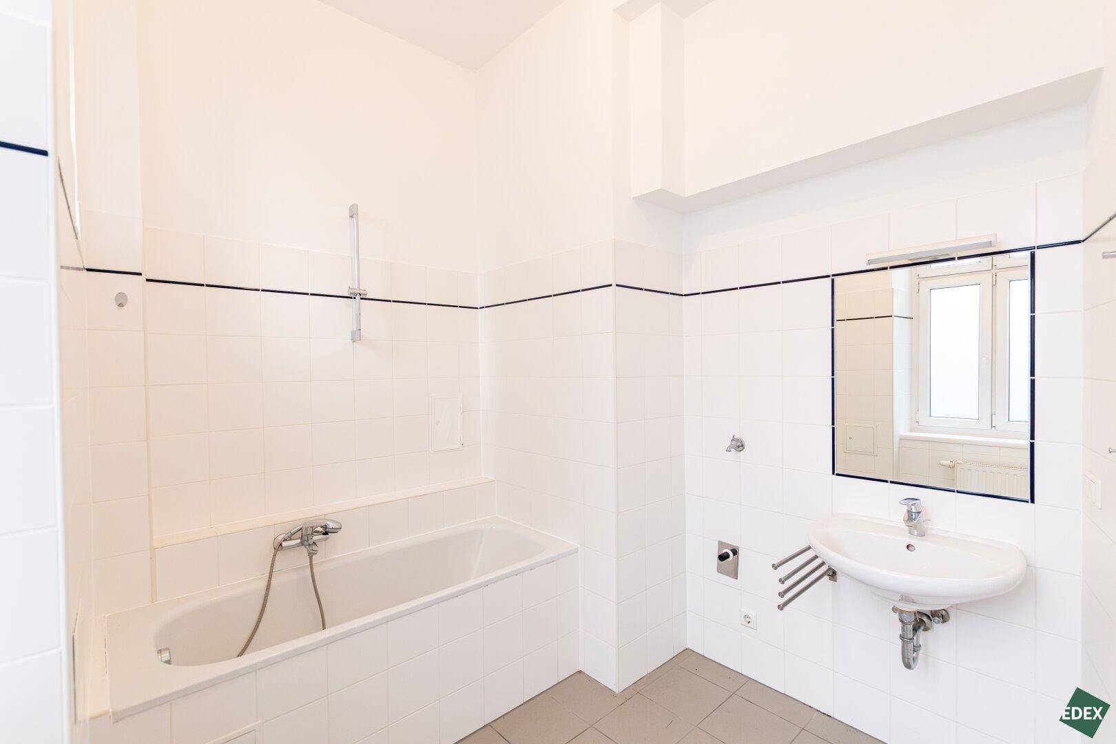 Helles Badezimmer mit Badewanne, Waschbecken und weißen Fliesen, inklusive Fenster.