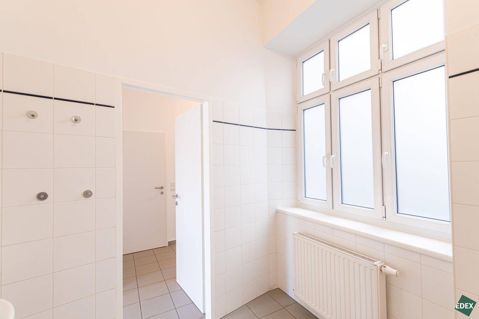 Geräumiges Badezimmer mit großen Fenstern, weißen Fliesen und viel Tageslicht.