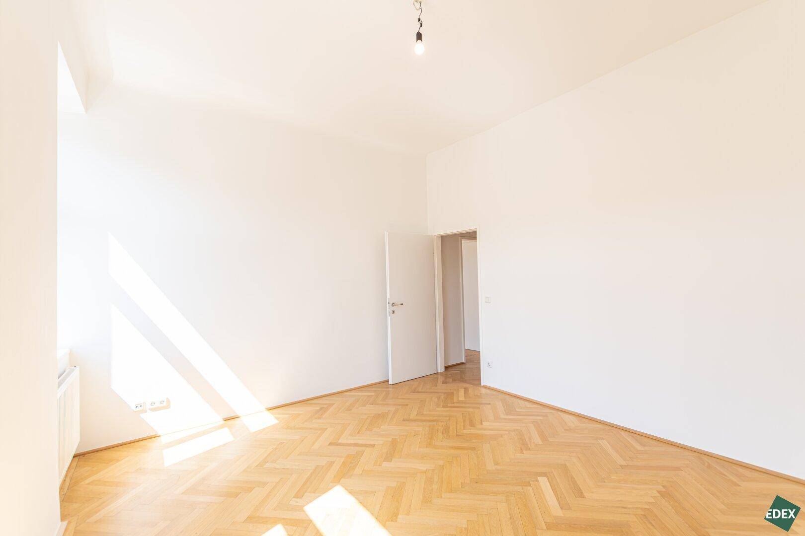 Leeres Zimmer mit Fischgrätparkett und weiß gestrichenen Wänden, bereit für die Einrichtung.