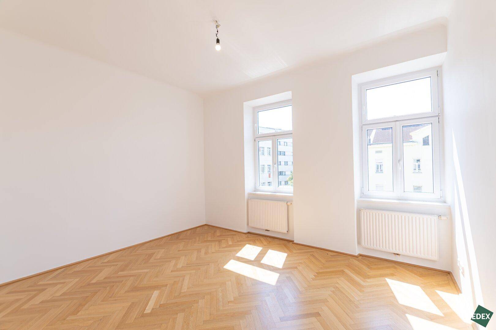 Geräumiges, helles Zimmer mit Fischgrätparkett und zwei großen Fenstern, die viel Licht spenden.