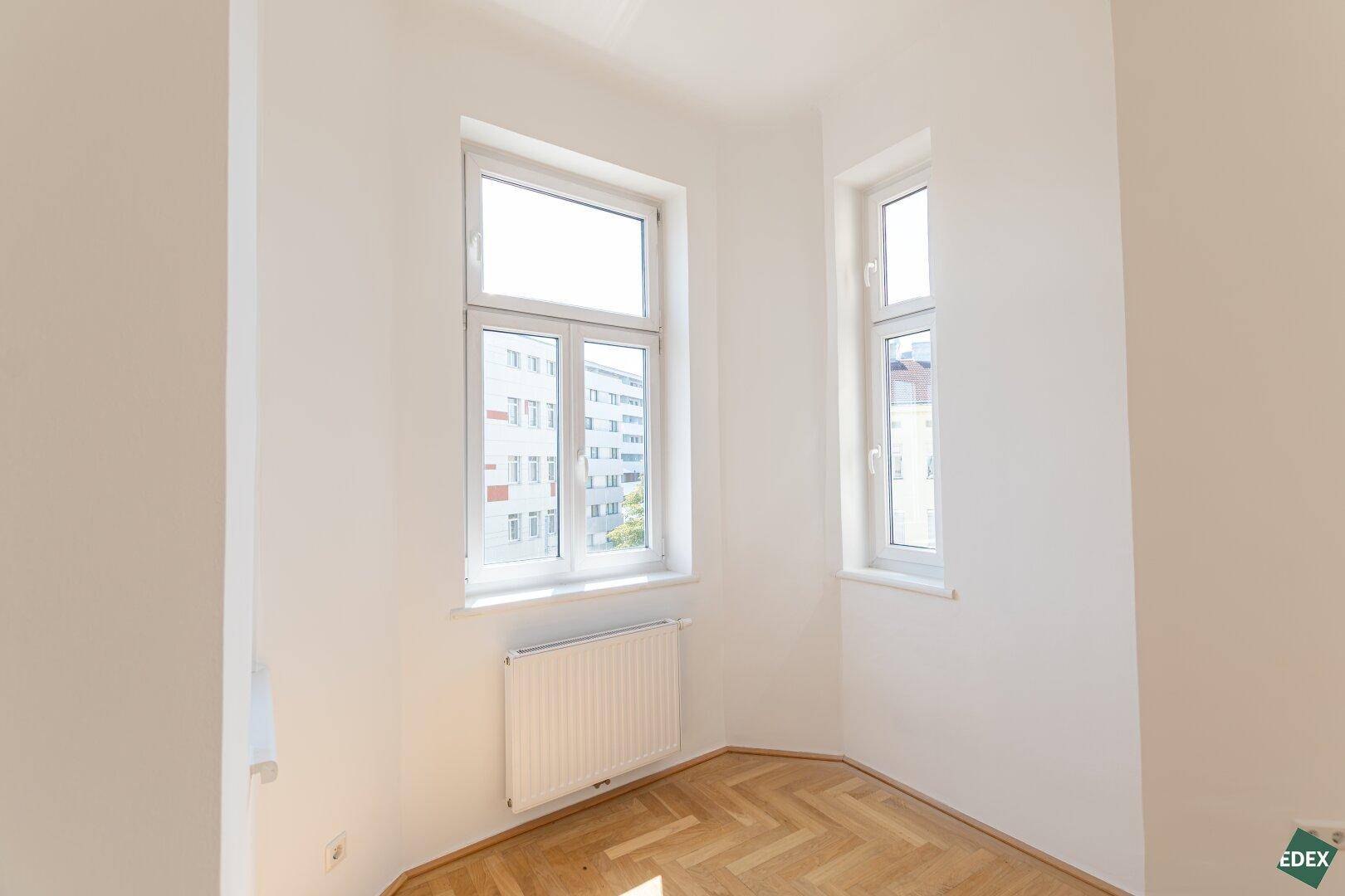 Kleineres Zimmer mit Fischgrätparkett und zwei Fenstern, ideal als Schlaf- oder Arbeitszimmer.