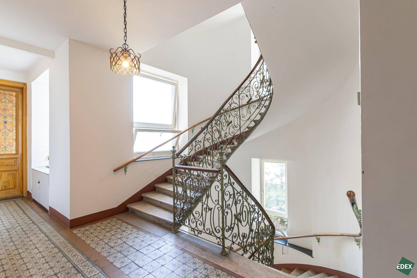 Historisches Treppenhaus mit schmiedeeisernem Geländer und verzierten Fliesen, klassischer Altbau-Stil.