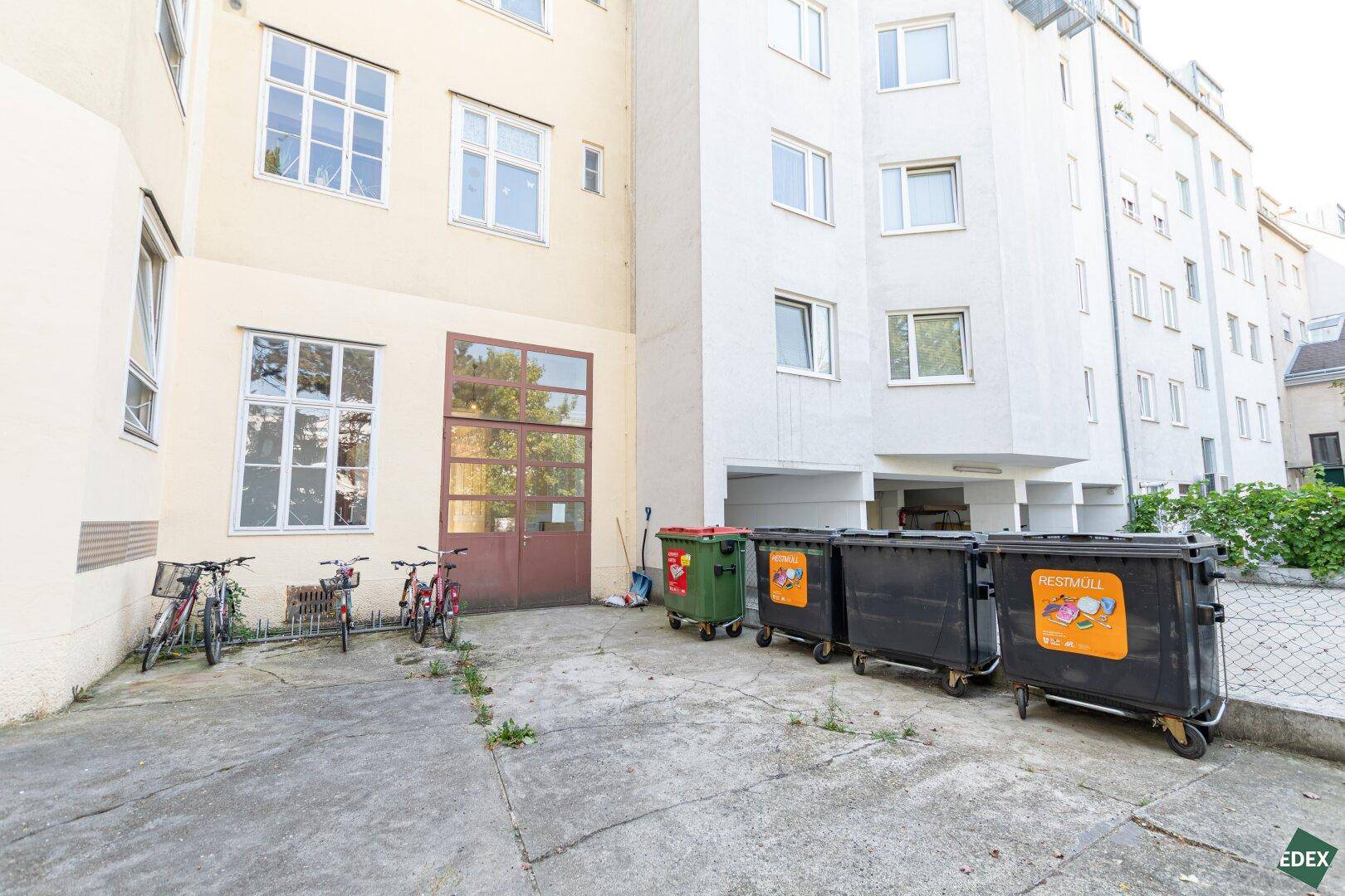 Hinterhofbereich mit Mülltonnen, Fahrrädern und Gebäudefassaden, funktionaler Außenbereich.