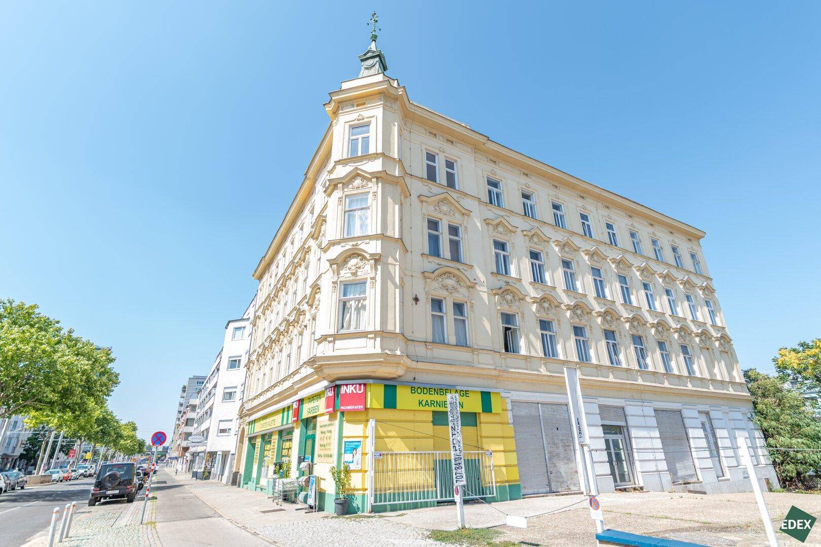 Historisches Eckgebäude mit reich verzierter Fassade und Geschäften im Erdgeschoss unter blauem Himmel.
