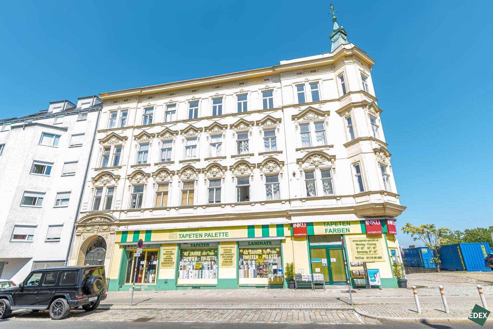 Detailansicht des historischen Eckgebäudes mit Geschäften und dekorativen Fassadenelementen bei Sonnenschein.