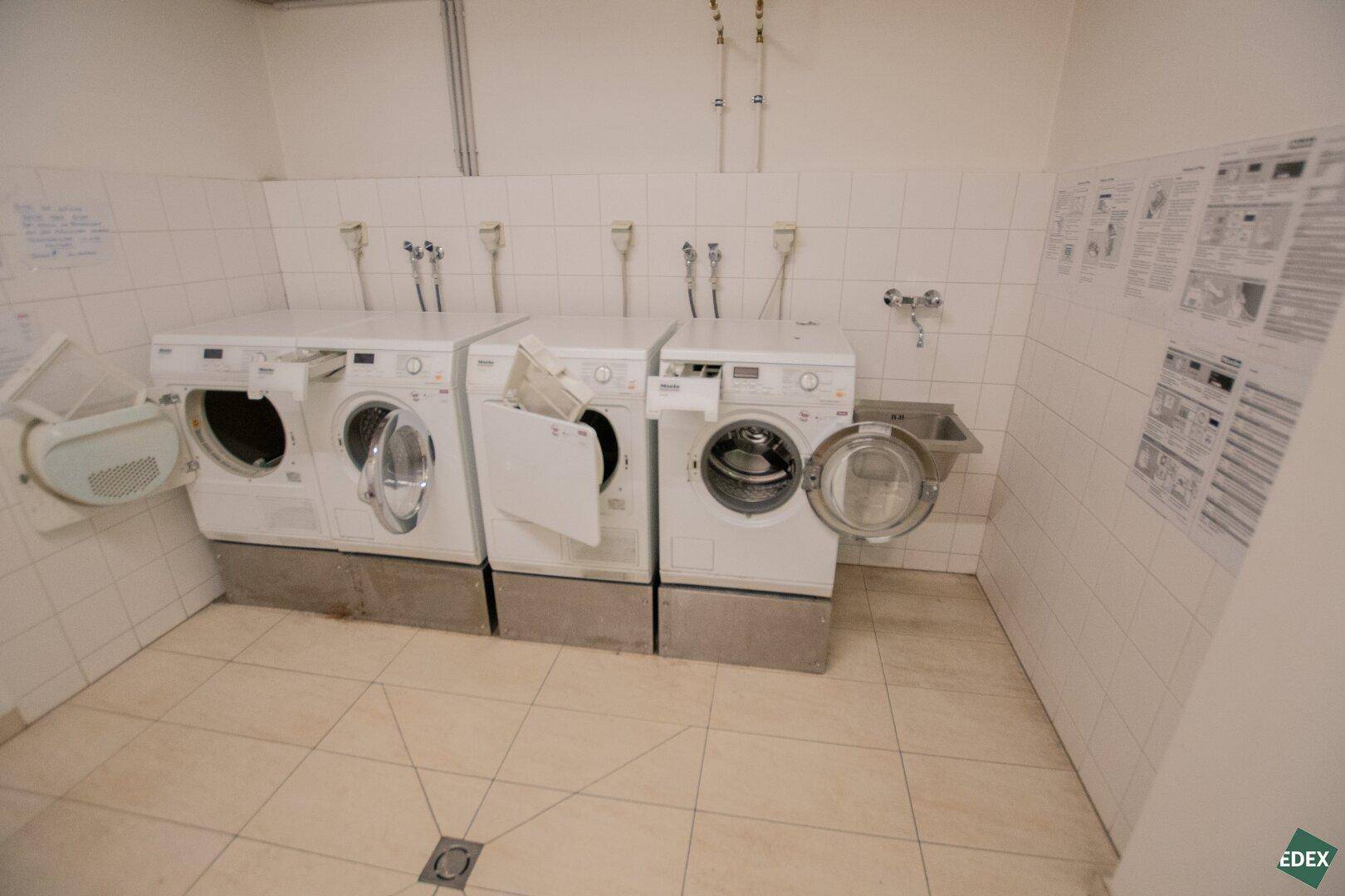 Gemeinschaftlicher Waschraum mit mehreren Waschmaschinen und einem Waschbecken.