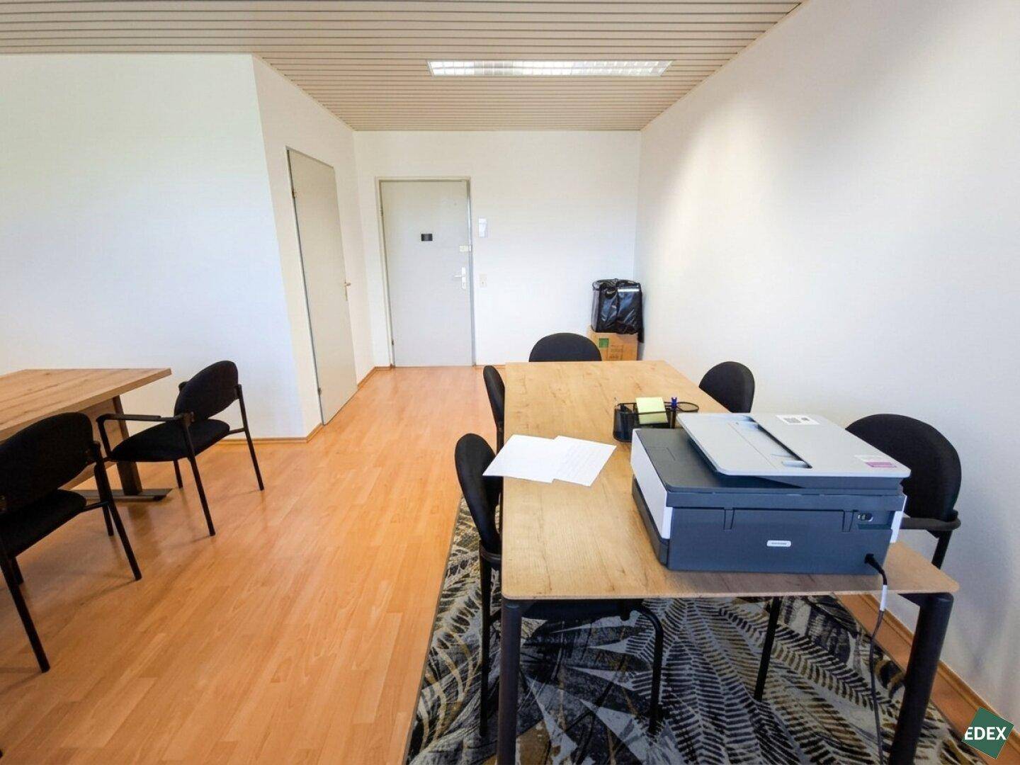 Bürobereich mit Drucker auf einem Tisch und zwei Türen im Hintergrund.