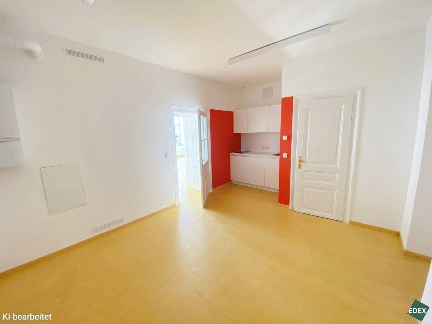 Kleine, moderne Küchenzeile mit weißen Schränken und roter Akzentwand in einem hellen Raum.