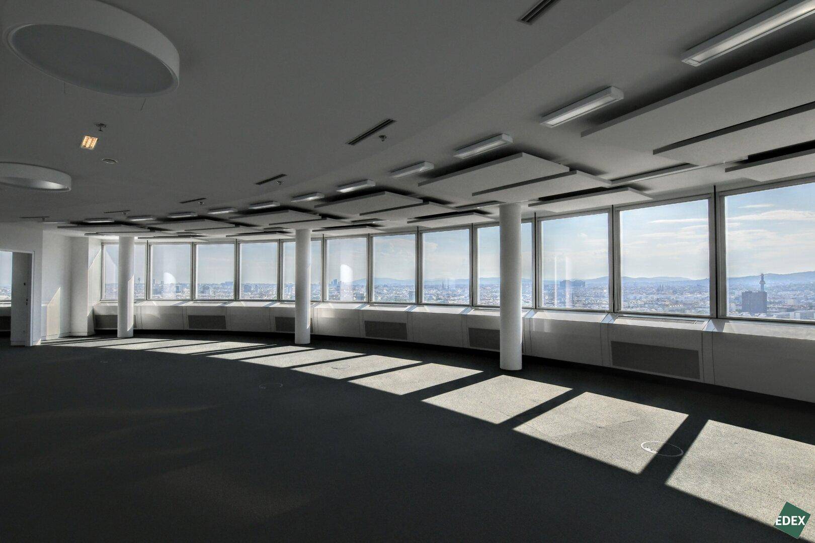 Heller Büroraum mit Teppichboden und Panoramablick durch die raumhohen Fenster.