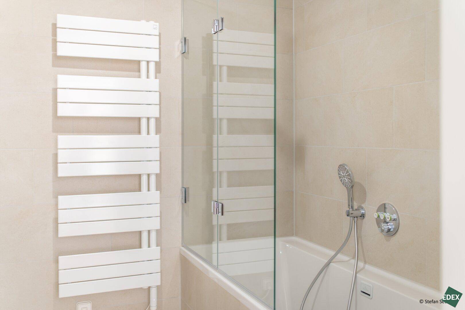 Modernes Badezimmer mit Badewanne, Duscharmatur und praktischem Handtuchheizkörper.