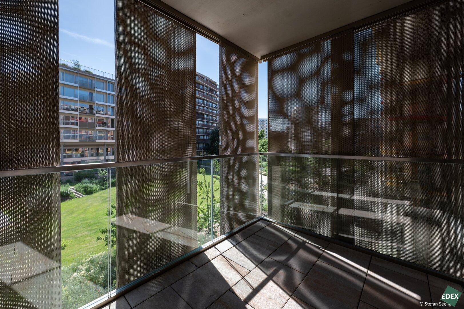 Heller Balkon mit Fliesenboden und Blick auf moderne Wohngebäude und Grünanlagen.