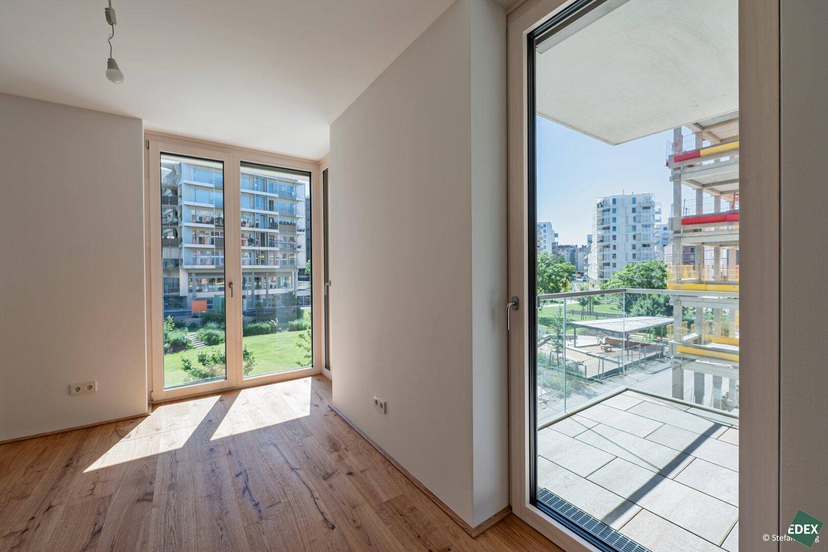 Lichtdurchfluteter Raum mit Holzboden und Zugang zu einem Balkon, bietet Ausblick.