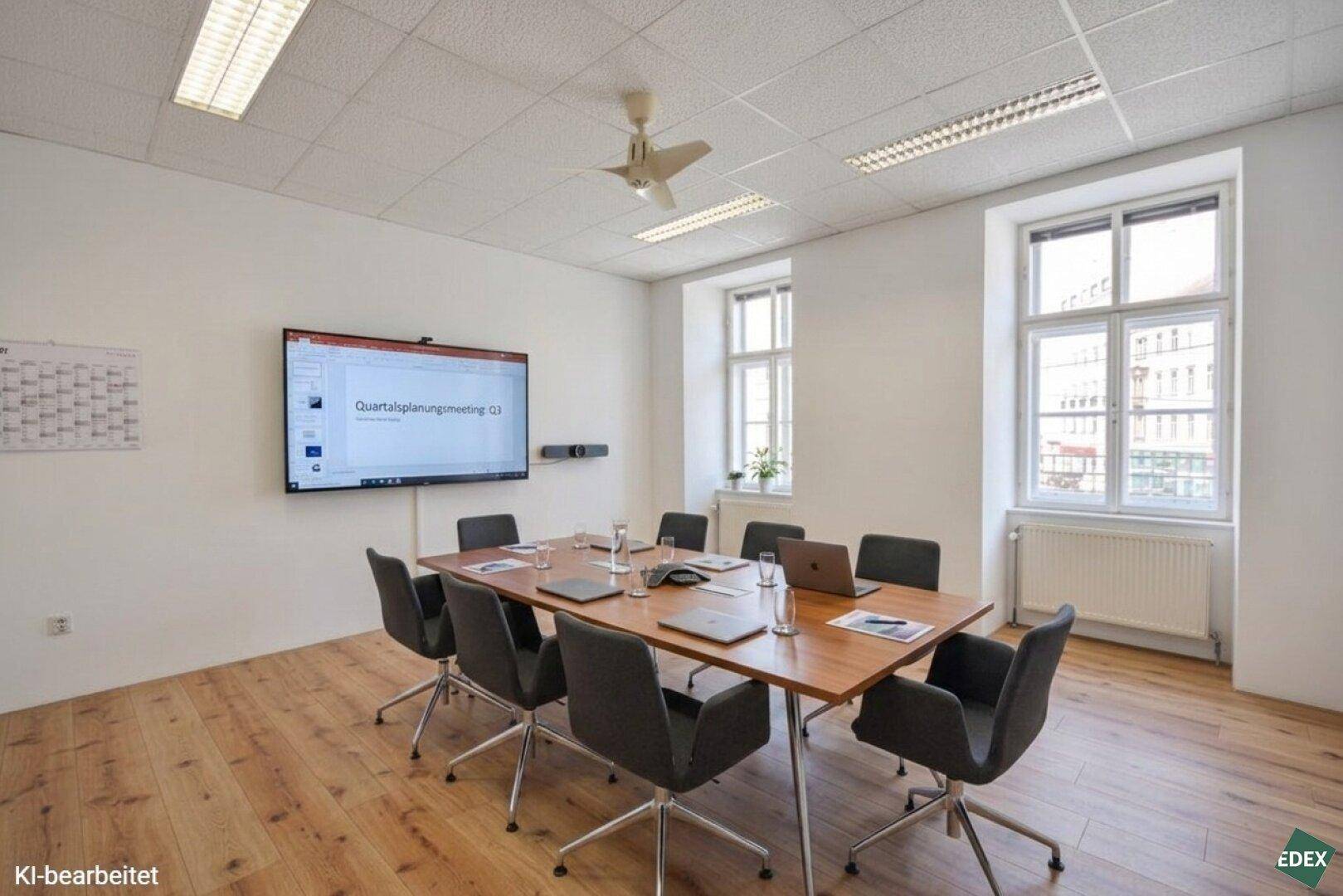 Moderner Konferenzraum mit großem Holztisch, bequemen Stühlen und einem Wandbildschirm für Präsentationen.