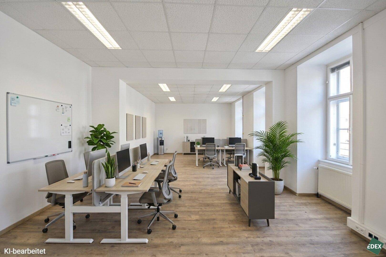 Geräumiges Büro mit mehreren Arbeitsplätzen, Whiteboard und Pflanzen, das viel natürliches Licht bietet.