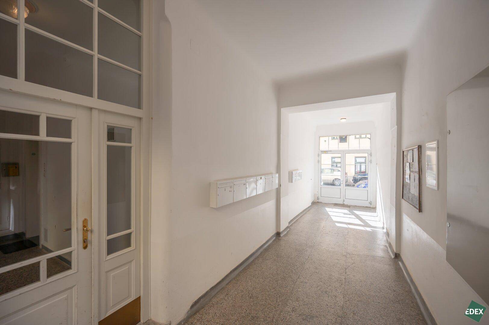 Heller Eingangsbereich mit Terrazzoboden und Zugang zum Treppenhaus und zur Straße.