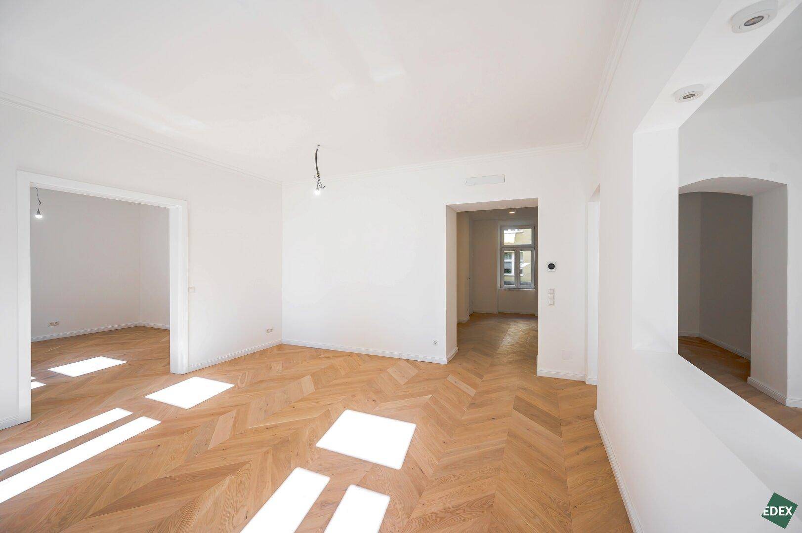Geräumiges, helles Zimmer mit Fischgrätparkett und Blick in angrenzende Räume.