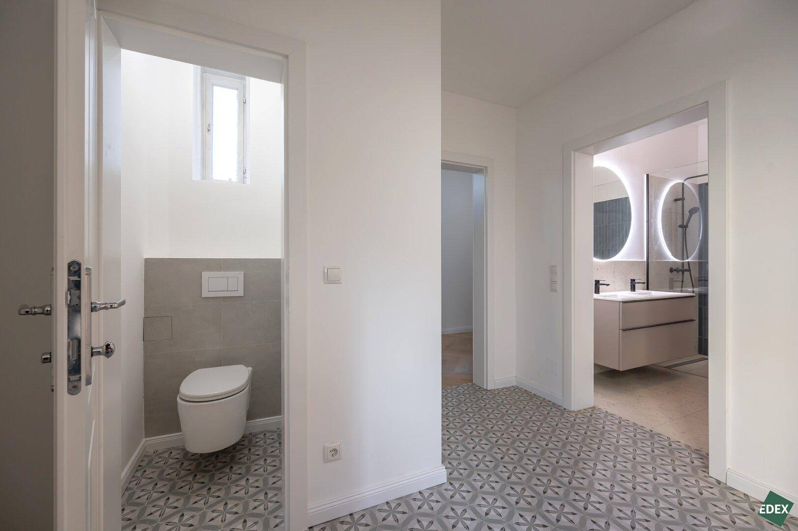 Separates Gäste-WC mit Wand-WC und kleinem Fenster, modern gefliest.
