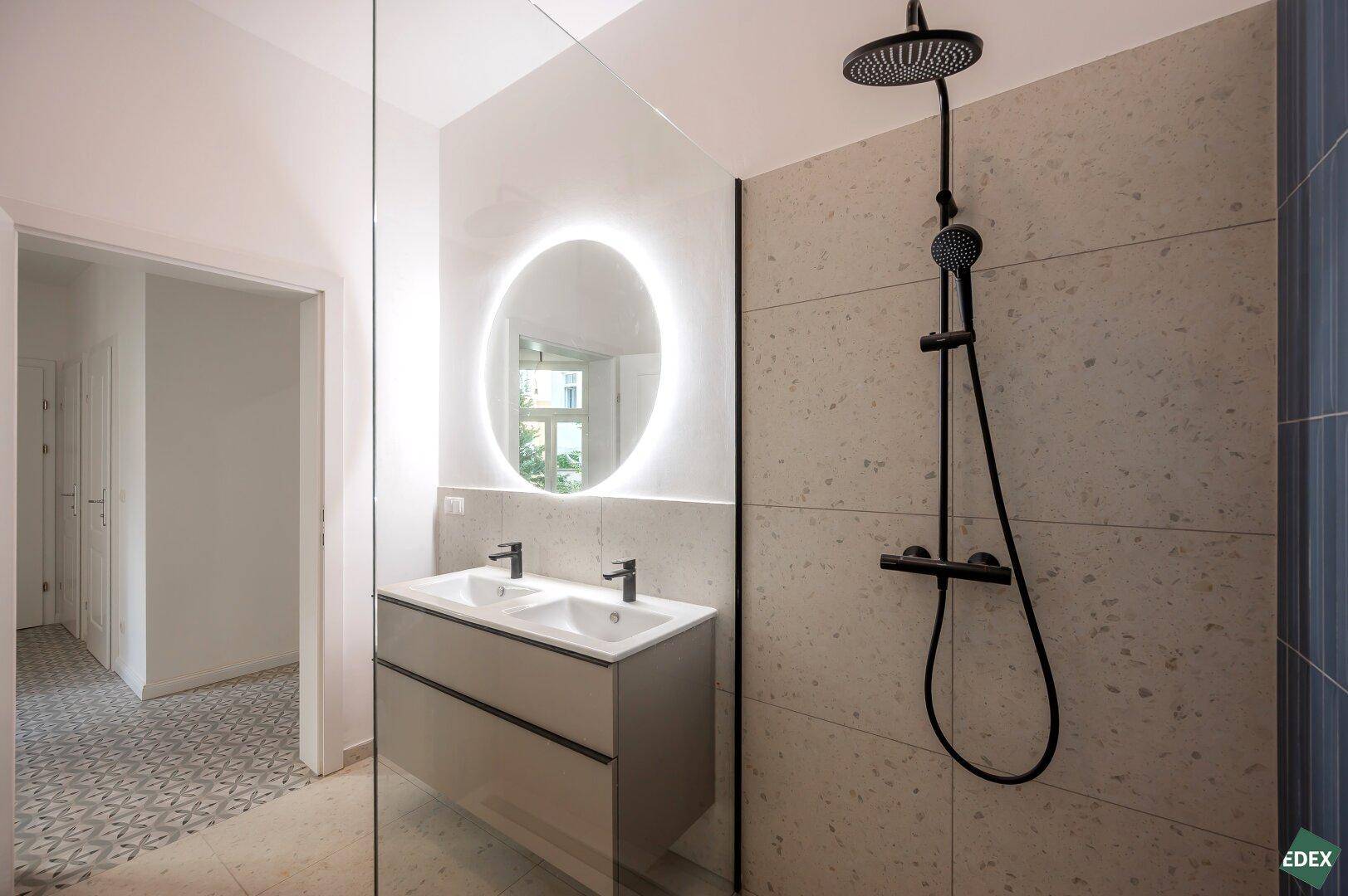 Elegantes Badezimmer mit Doppelwaschbecken, beleuchtetem Spiegel und Regendusche.