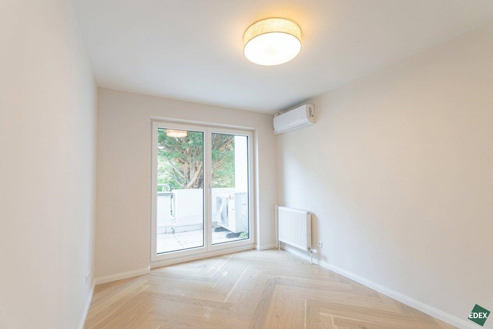 Helles Zimmer mit Holzboden, Klimaanlage und Zugang zu einem kleinen Außenbereich.
