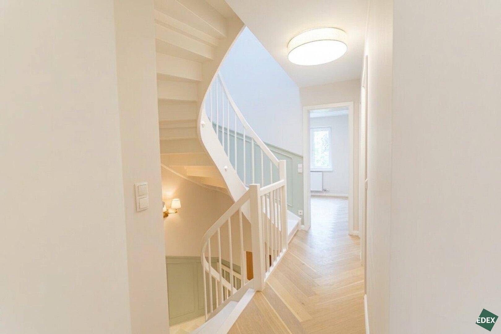 Eleganter Flur mit geschwungener Treppe, Holzboden und heller Wandgestaltung.