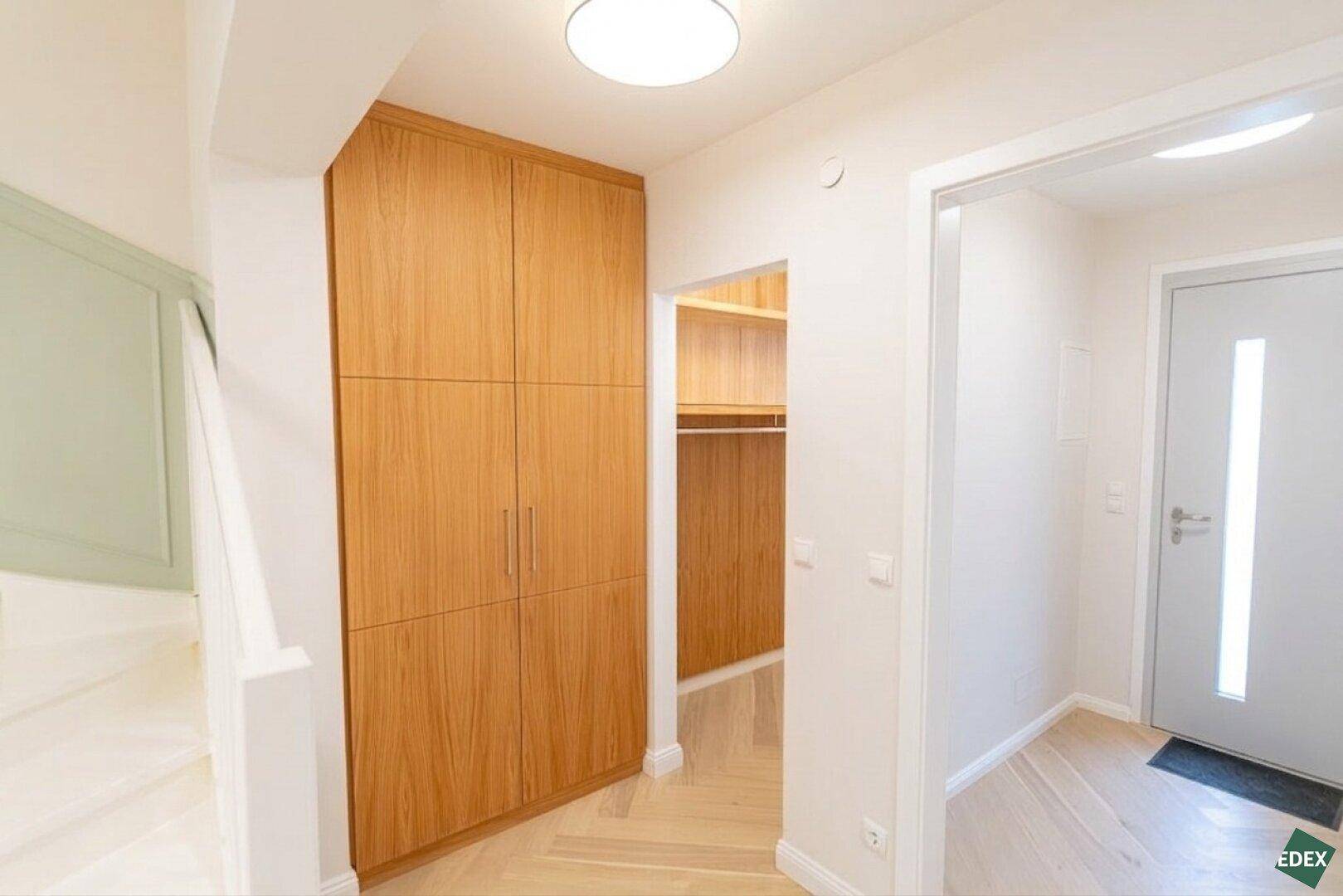 Eingangsbereich mit Einbauschränken aus Holz, Holzboden und Zugang zur Treppe.