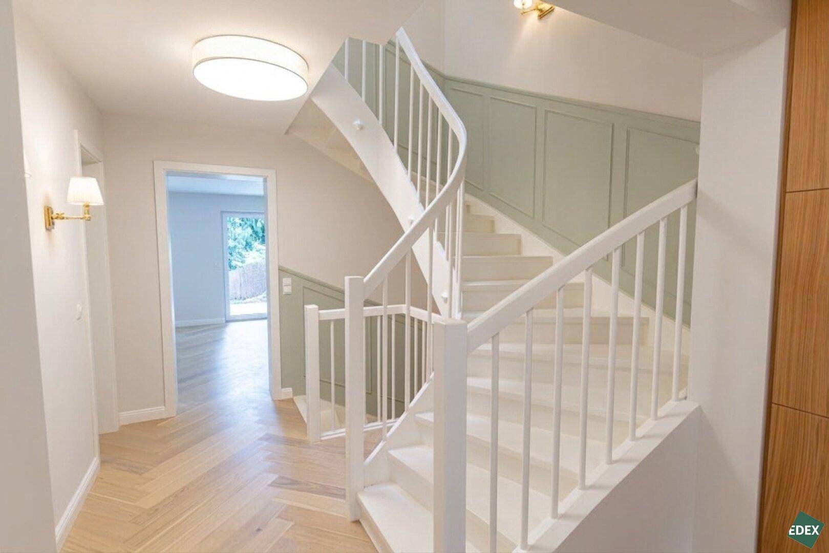 Heller Flur mit eleganter, geschwungener Treppe und Holzboden, modern gestaltet.