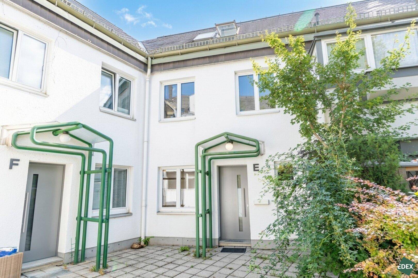 Weiße Gebäudefassade mit mehreren Eingängen und einem gepflasterten Vorplatz.