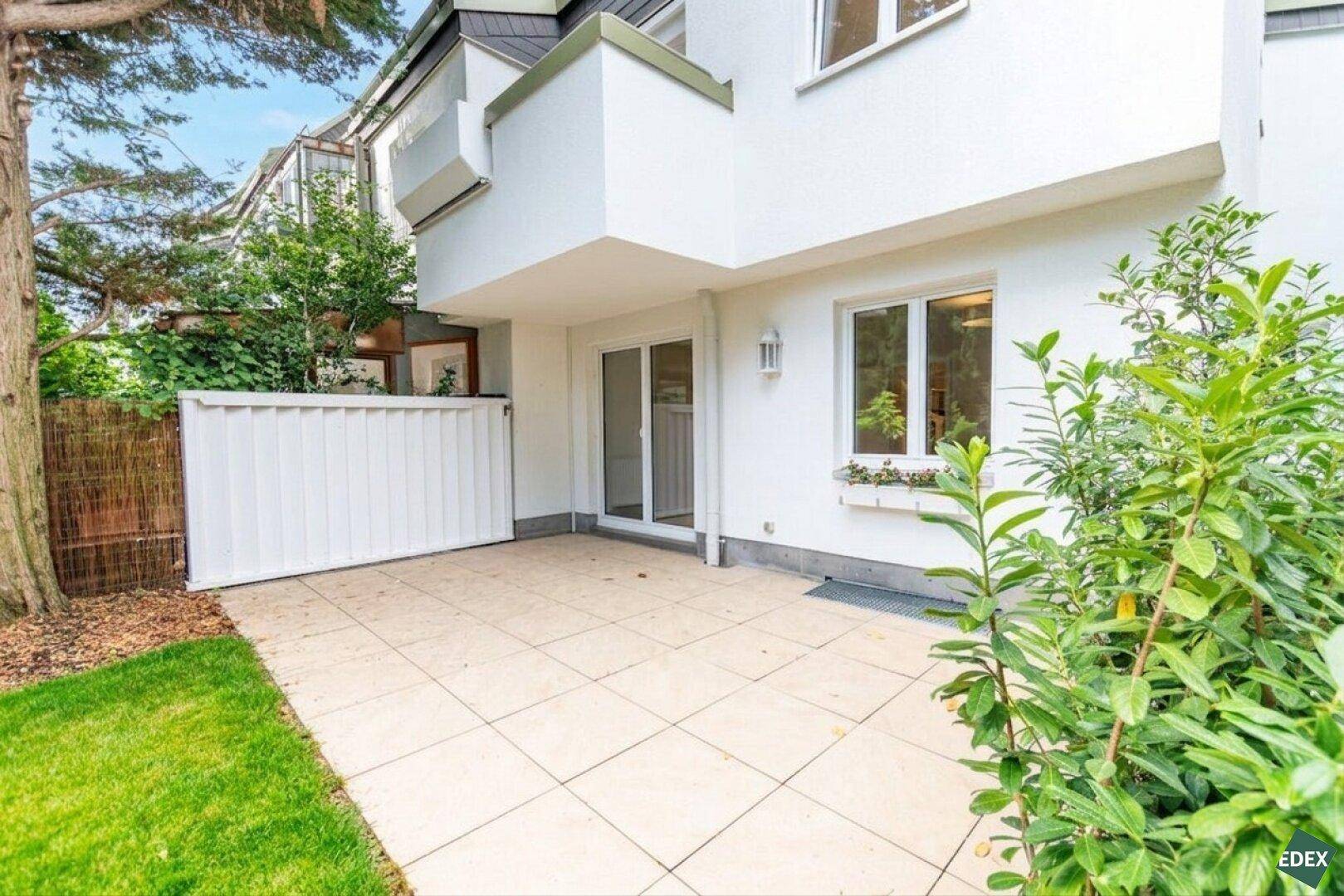 Geflieste Terrasse am Haus mit Zugang zum Garten und viel Grün drumherum.