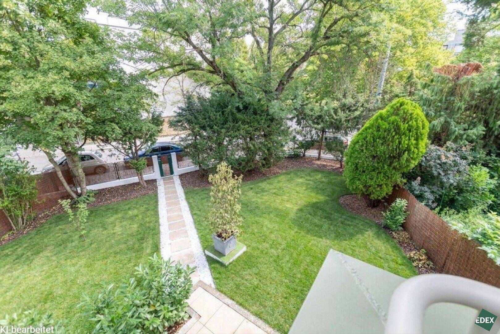 Blick von oben auf den weitläufigen Garten mit Rasen, Bäumen und einem Steinweg.