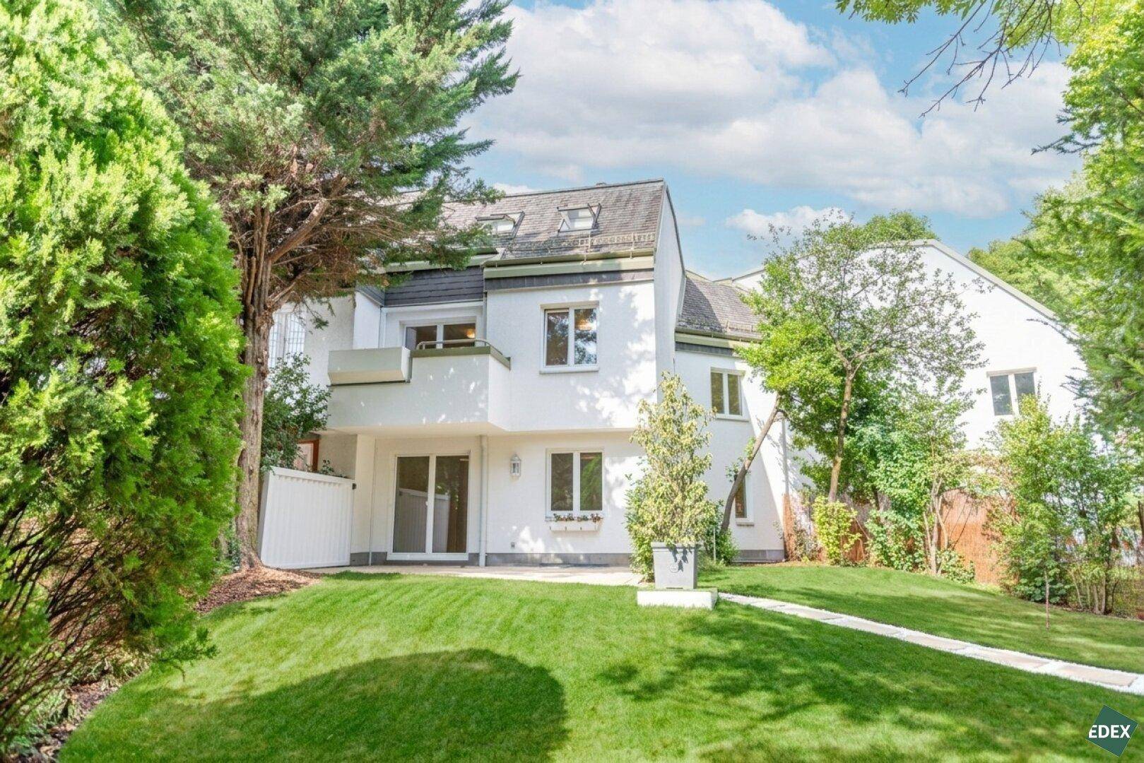 Attraktives Wohnhaus mit weißer Fassade, Balkon und großem, sonnigen Gartenbereich.