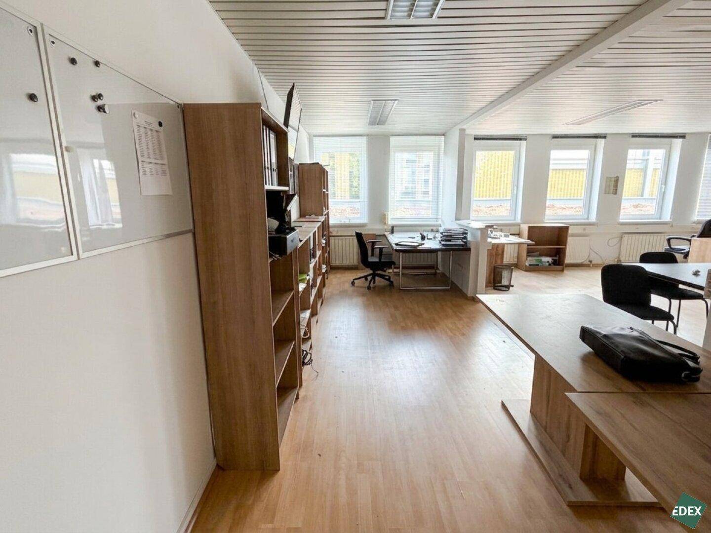 Großzügiger offener Bürobereich mit mehreren Arbeitsplätzen, Holzregalen und vielen Fenstern für viel Tageslicht.