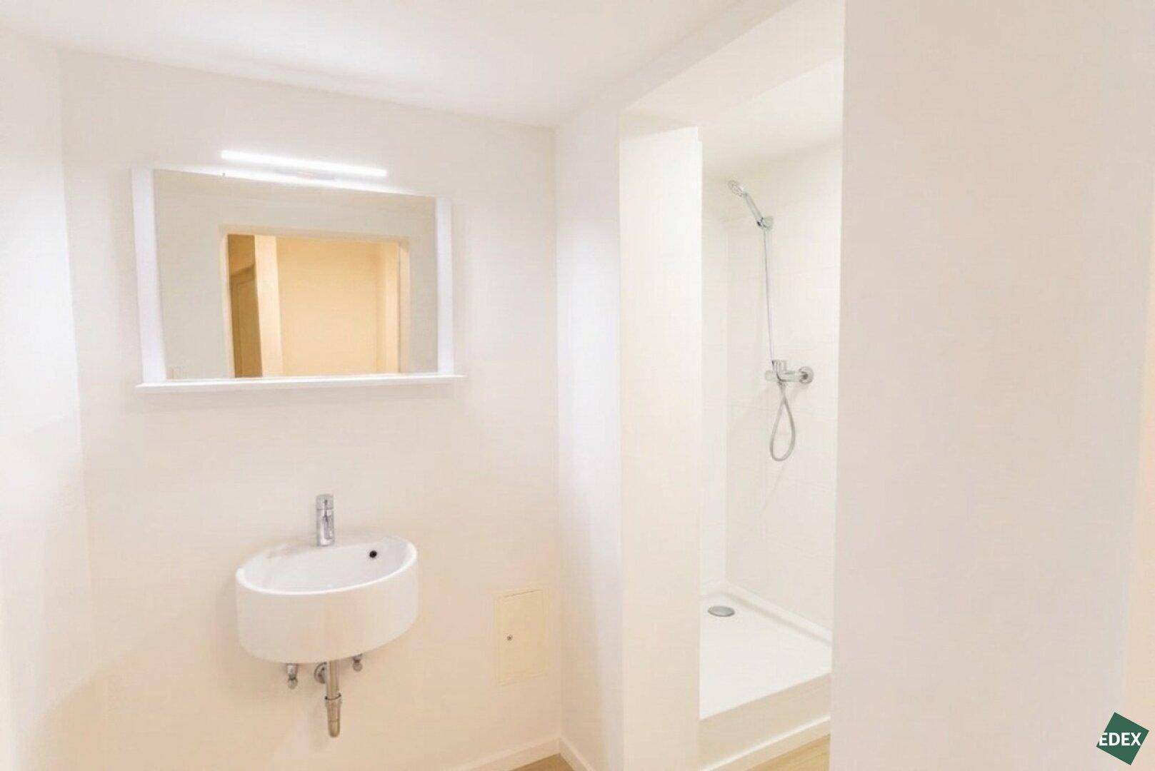 Modernes Badezimmer mit Dusche, Waschbecken und Spiegel, in hellen Tönen gehalten.