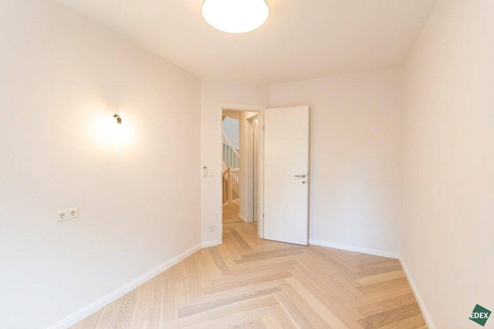 Helles, unmöbliertes Zimmer mit Holzboden und Zugang zum Flur.
