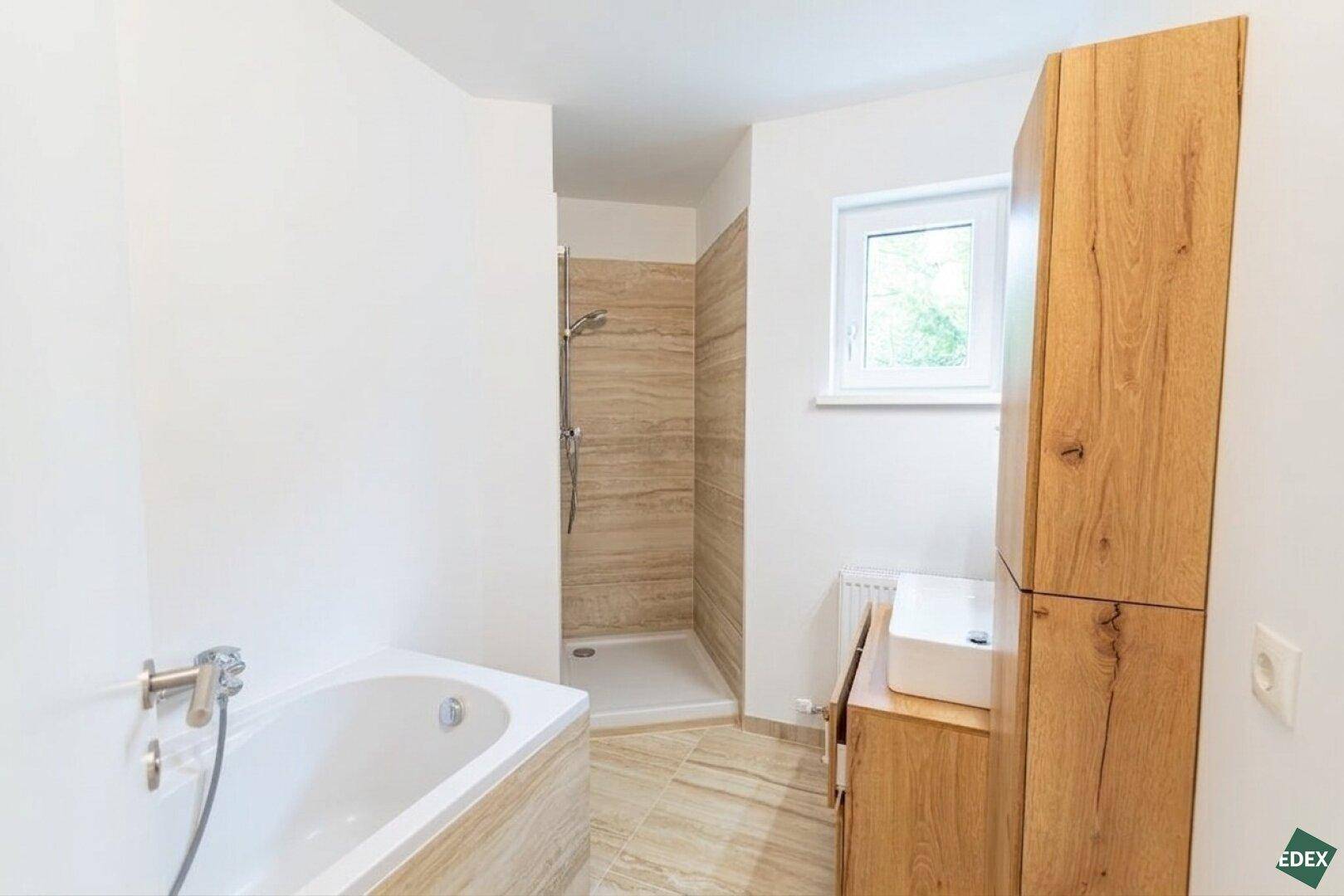 Helles Badezimmer mit Badewanne, Dusche, Holzmöbeln und Fenster für Tageslicht.