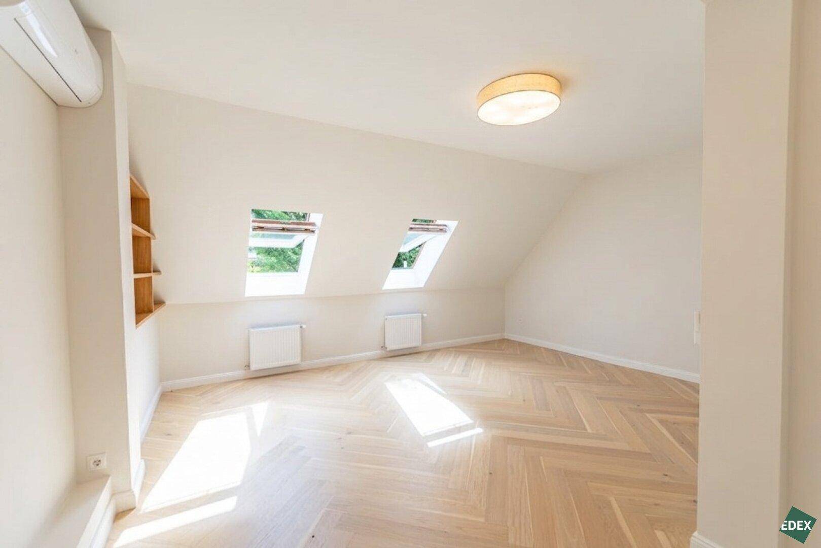 Helles Dachgeschosszimmer mit schrägen Wänden, Holzboden und zwei Dachfenstern.