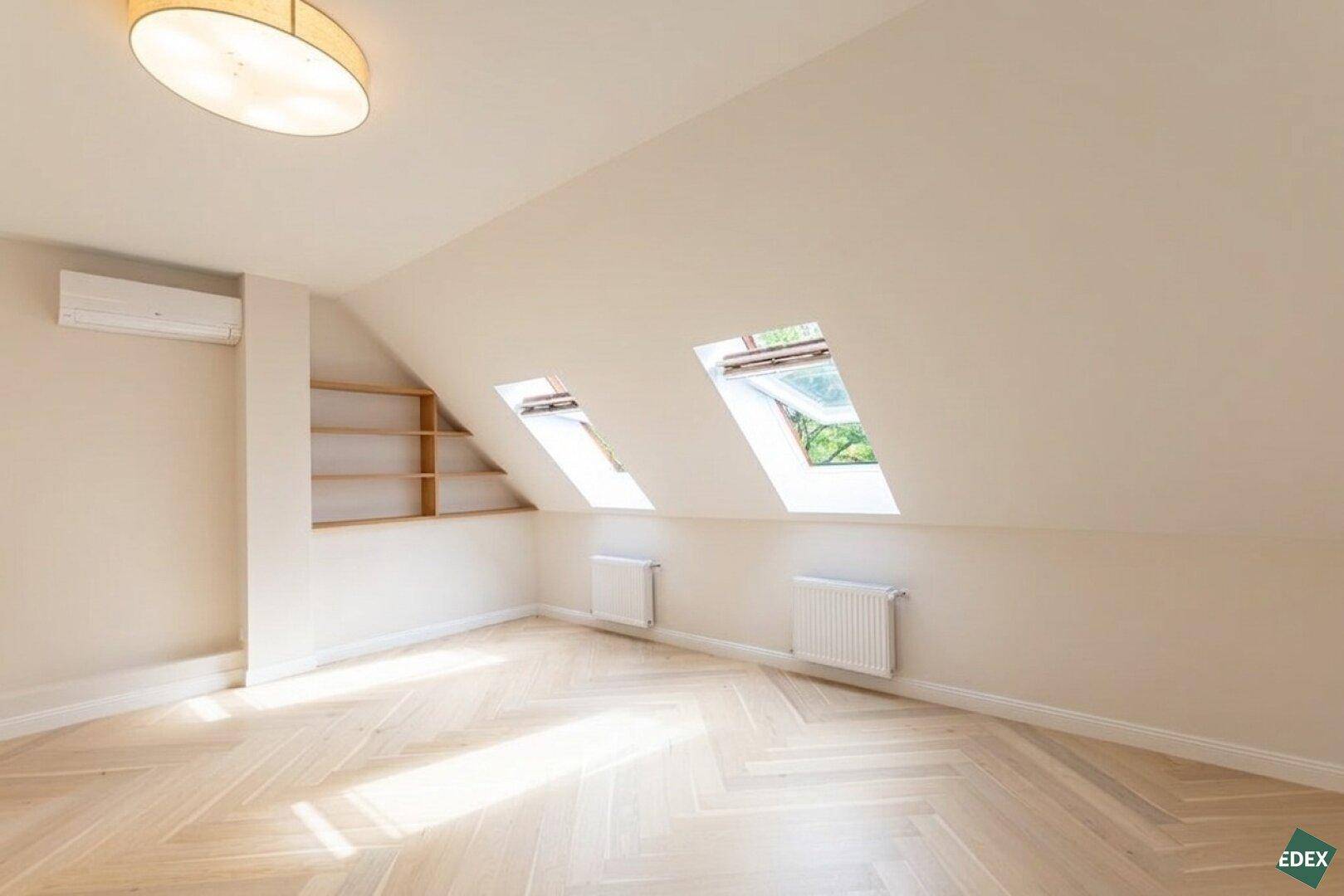 Helles Dachgeschosszimmer mit Schrägdach, Dachfenstern und Fischgrätparkettboden.