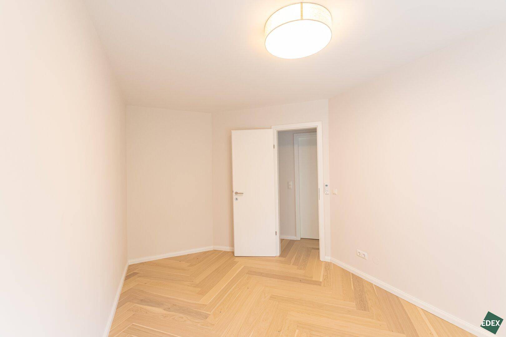 Helles, unmöbliertes Zimmer mit Holzboden und Zugang zu einem weiteren Raum.