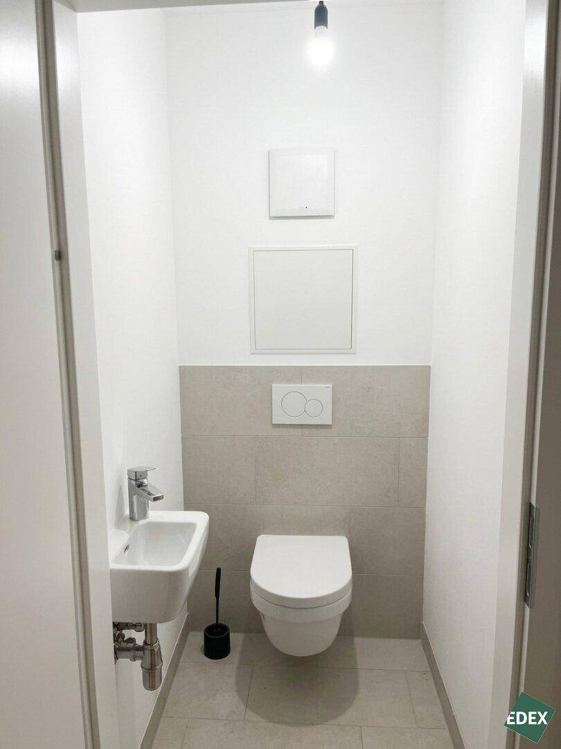 Separates Gäste-WC mit wandhängendem WC und kleinem Handwaschbecken.
