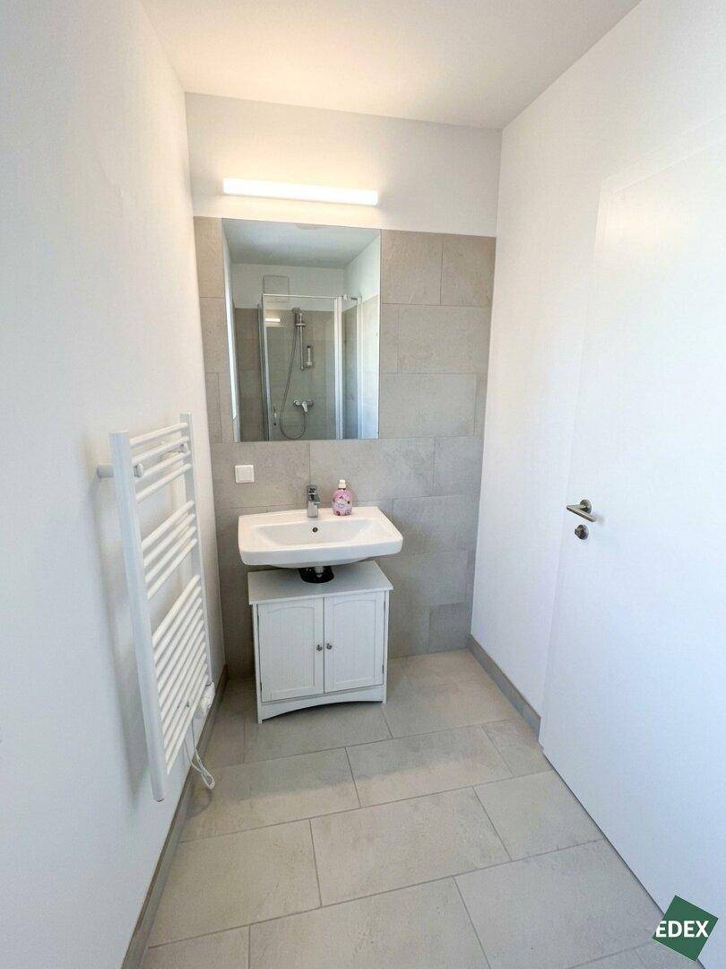 Modernes Badezimmer mit Dusche, Waschbecken und hellen Fliesen.