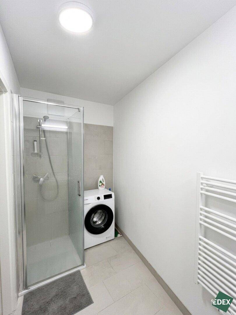 Helles Badezimmer mit Duschkabine, Waschmaschine und beheiztem Handtuchhalter.