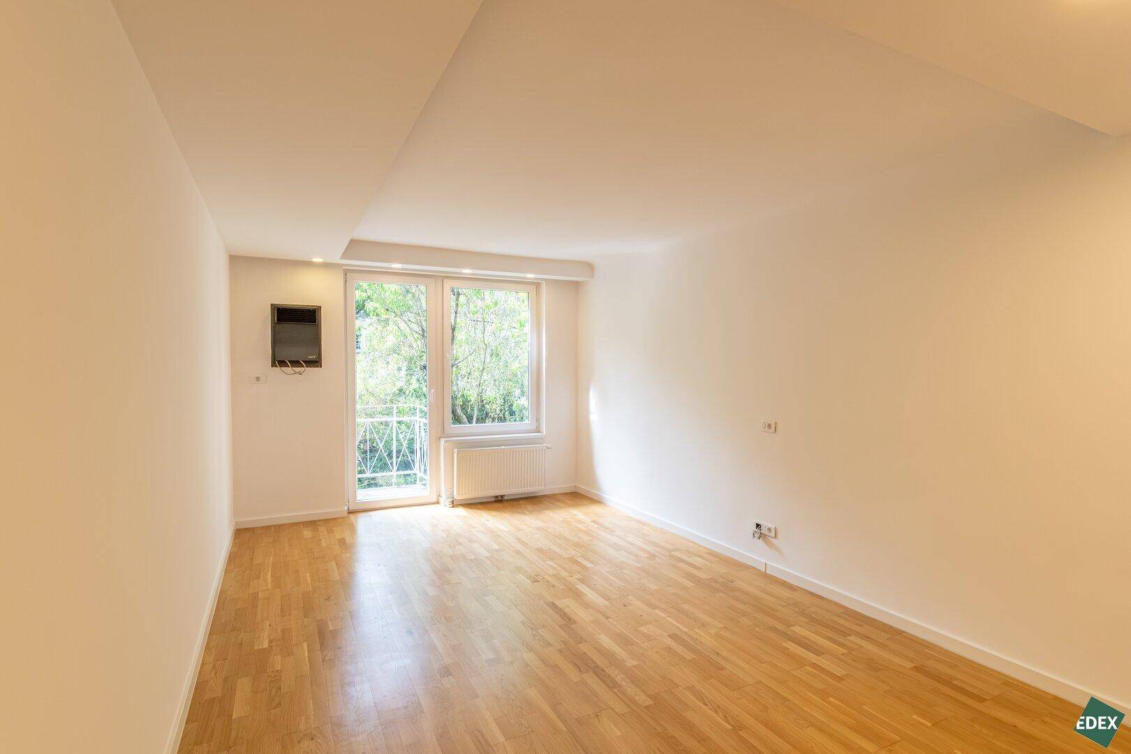 Geräumiges, helles Wohnzimmer mit Parkettboden und Zugang zu einem französischen Balkon.